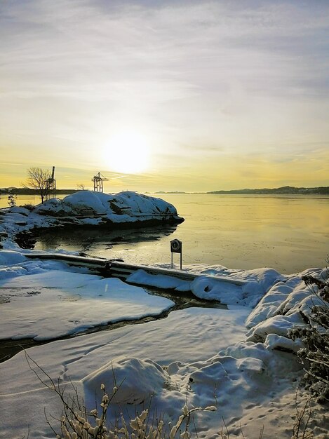 Imagen vertical de una isla cubierta de nieve rodeada por el mar durante la puesta de sol en Noruega