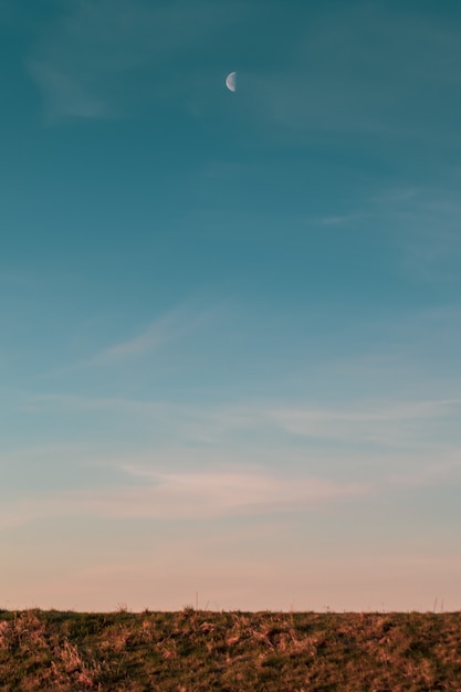 Imagen vertical de la luna y el cielo azul sobre un campo durante la puesta de sol por la noche