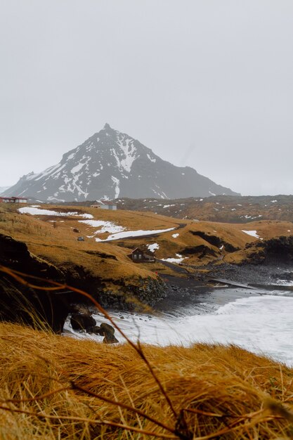 Imagen vertical de un río rodeado por colinas cubiertas de nieve y vegetación en Islandia