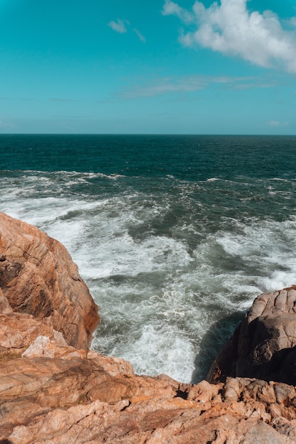 Imagen vertical de rocas rodeadas por el mar bajo un cielo azul y la luz del sol