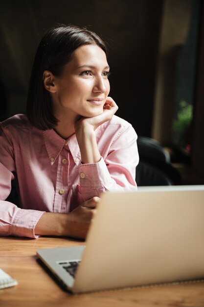 Imagen vertical de la sonriente mujer morena sentada junto a la mesa