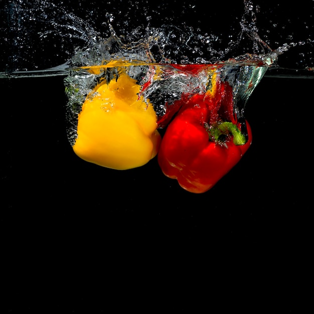 Impacto de pimiento cayendo al agua sobre fondo negro