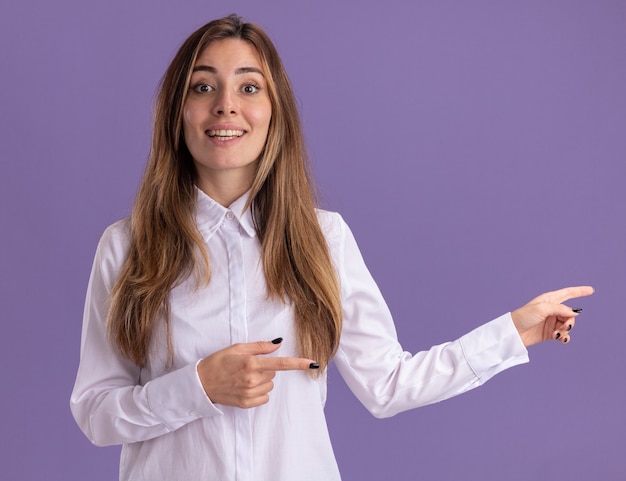 Impresionada joven bastante caucásica apunta al lado con las dos manos en púrpura