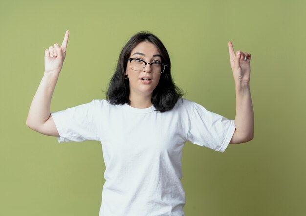 Impresionada joven bastante caucásica con gafas apuntando hacia arriba aislado sobre fondo verde oliva