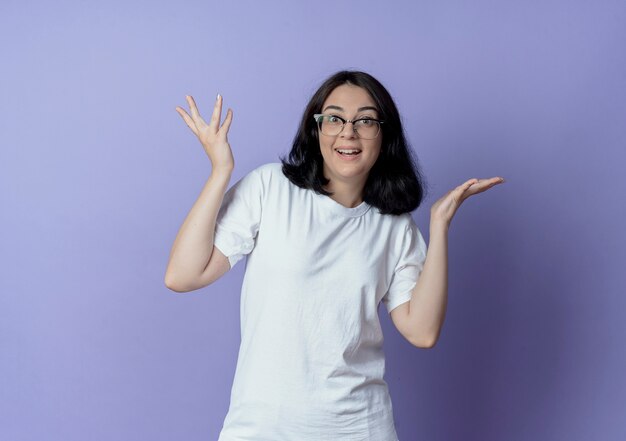 Impresionada joven bastante caucásica con gafas y mostrando las manos vacías aisladas sobre fondo púrpura con espacio de copia