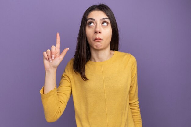 Impresionada joven bastante caucásica mirando y apuntando hacia arriba aislado en la pared púrpura con espacio de copia