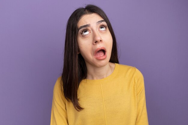 Impresionada joven bastante caucásica mirando hacia arriba aislado en la pared púrpura con espacio de copia