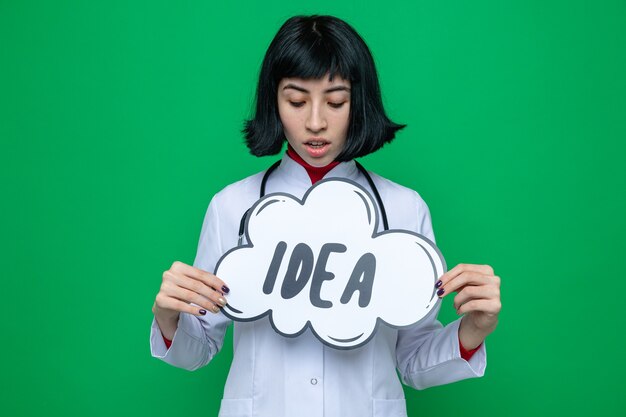 Foto gratuita impresionada joven bastante caucásica en uniforme médico con estetoscopio sosteniendo y mirando la burbuja de la idea