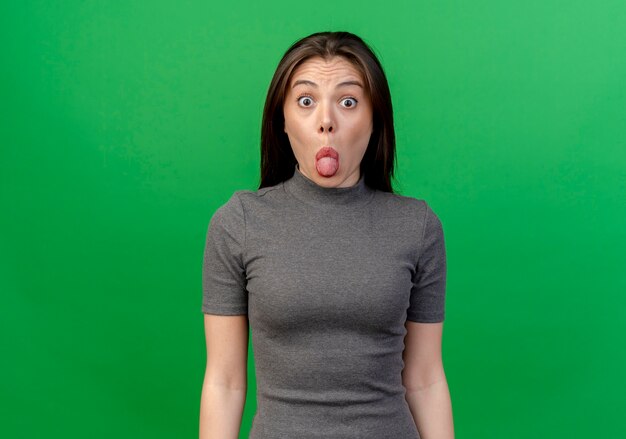 Impresionada joven bonita mostrando la lengua a la cámara aislada en verde con espacio de copia