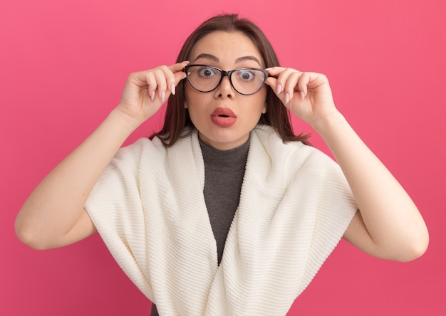 Impresionada joven bonita a mujer vistiendo y agarrando gafas