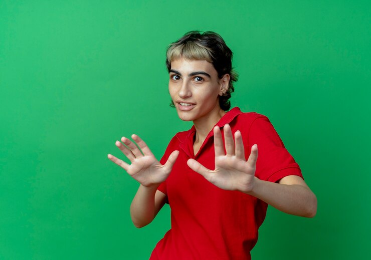 Foto gratuito impresionada joven caucásica con corte de pelo pixie estirando las manos gesticulando no aislado sobre fondo verde con espacio de copia
