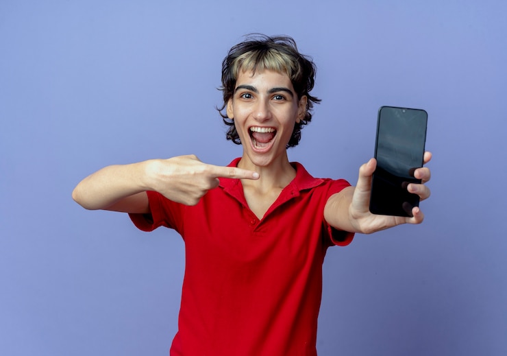 Foto gratuito impresionada joven caucásica con corte de pelo pixie sosteniendo estirando y apuntando al teléfono móvil aislado sobre fondo púrpura