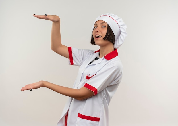 Impresionada joven cocinera en uniforme de chef aislado en blanco con espacio de copia