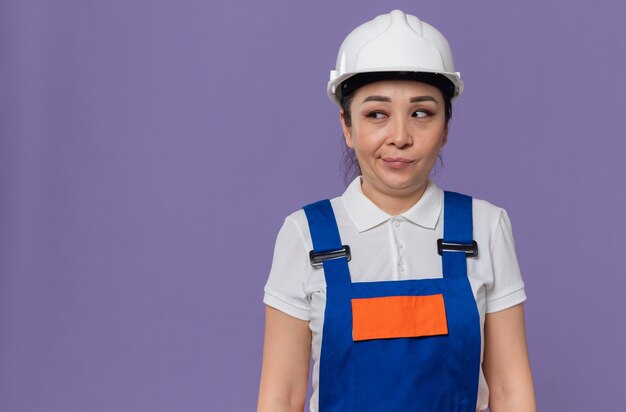 Impresionada joven constructora asiática con casco de seguridad blanco mirando al lado