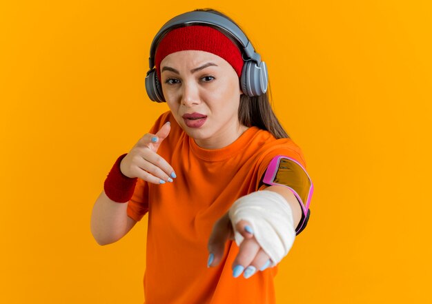 Impresionada joven deportiva con diadema y muñequeras y auriculares