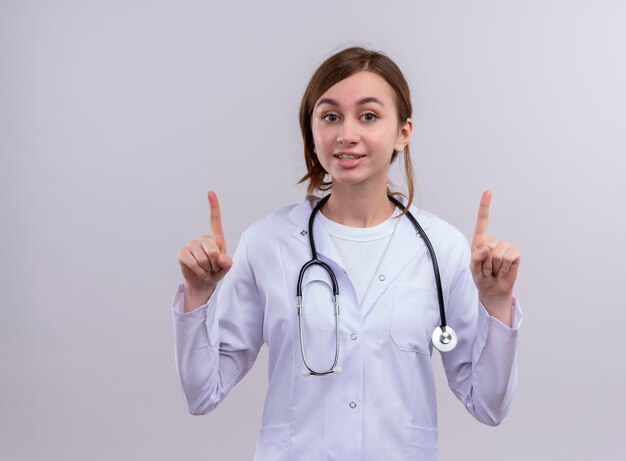 Impresionada joven doctora vistiendo bata médica y un estetoscopio con los dedos levantados con espacio de copia