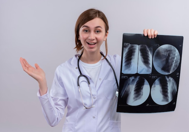 Impresionada joven doctora vistiendo bata médica y un estetoscopio y sosteniendo una radiografía