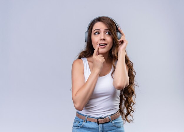 Impresionada joven hermosa con audífonos mirando el lado derecho con el dedo en el labio con espacio de copia