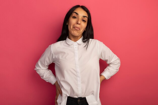 Impresionada joven hermosa mujer vestida con camiseta blanca poniendo la mano en la cadera