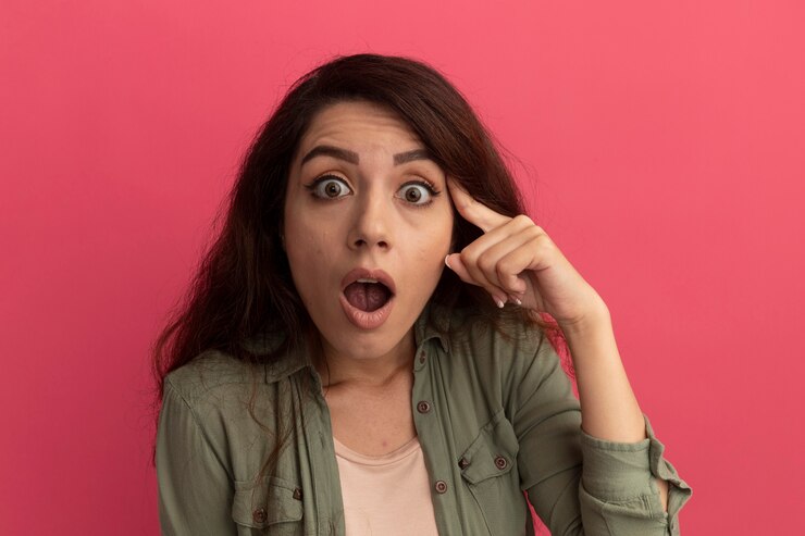 Foto gratuito impresionada joven hermosa vestida con camiseta verde oliva poniendo el dedo en la sien aislado en la pared rosa