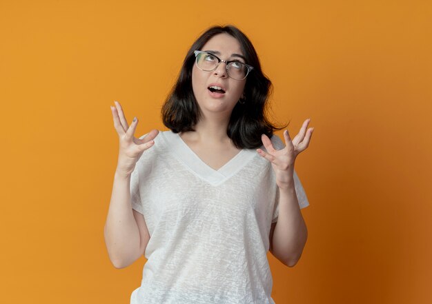 Impresionada joven mujer bonita con gafas mirando hacia arriba y manteniendo las manos en el aire