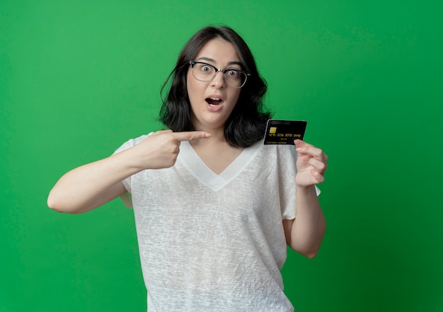 Foto gratuita impresionada joven mujer bonita con gafas sosteniendo y apuntando al teléfono móvil