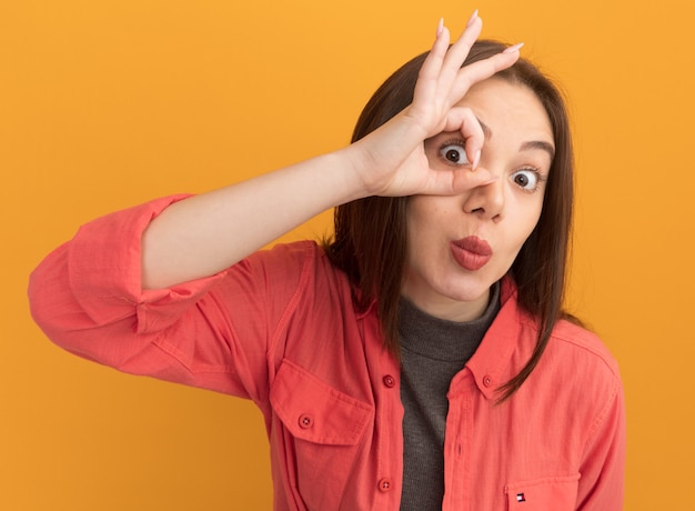 Foto gratuita impresionada joven mujer bonita haciendo gesto de mirada aislado en la pared naranja