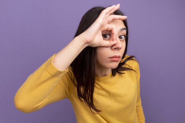 Impresionada joven mujer bonita mirando al frente haciendo gesto de mirada aislado en la pared púrpura