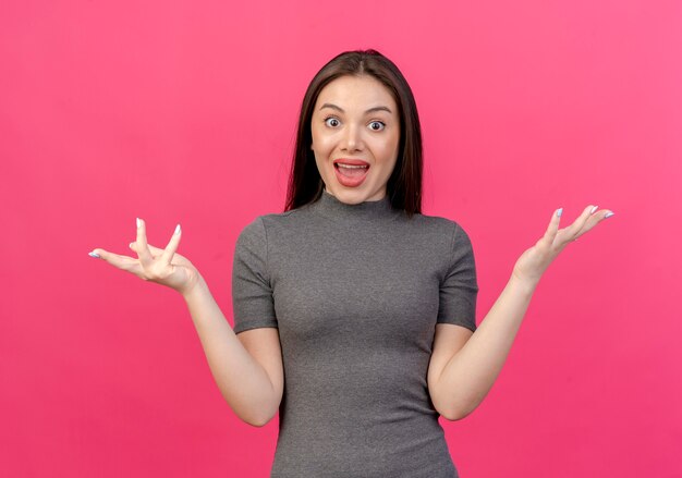 Impresionada joven mujer bonita mostrando las manos vacías aisladas sobre fondo rosa con espacio de copia