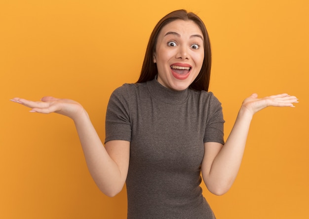 Impresionada joven mujer bonita mostrando las manos vacías mirando al frente aislado en la pared naranja