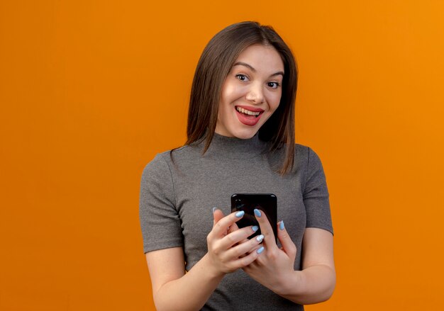 Impresionada joven mujer bonita sosteniendo teléfono móvil aislado sobre fondo naranja con espacio de copia