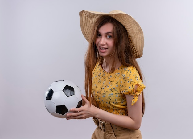 Impresionada joven con sombrero sosteniendo un balón de fútbol en un espacio en blanco aislado