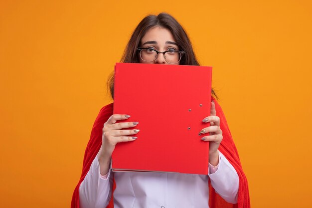 Impresionada joven superhéroe caucásica en capa roja vistiendo uniforme médico y estetoscopio