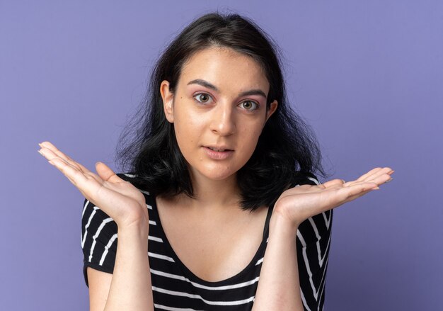 Impresionada mirada hermosa joven extendiendo las manos aisladas en la pared azul