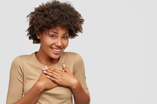 Impresionada mujer agradecida mantiene ambas manos en el pecho