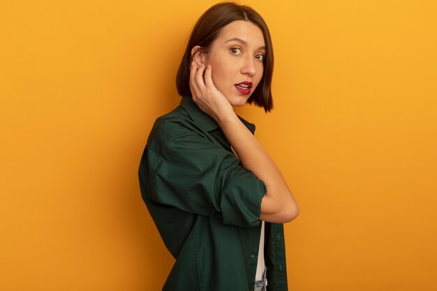 Impresionada mujer bonita caucásica se encuentra de lado pone la mano en la cara en naranja