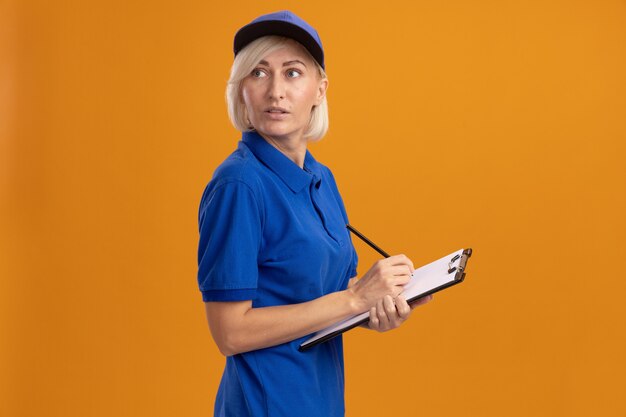 Impresionada mujer de entrega rubia de mediana edad en uniforme azul y gorra