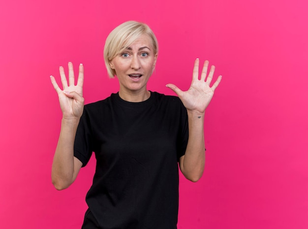 Impresionada mujer eslava rubia de mediana edad mirando al frente mostrando nueve con las manos aisladas en la pared rosa con espacio de copia