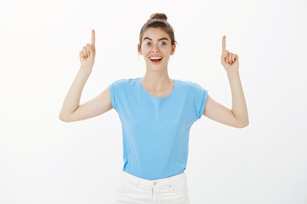 Impresionada mujer feliz apuntando con el dedo hacia arriba, mostrando publicidad con sonrisa alegre