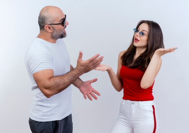 Foto gratuita impresionada pareja adulta con gafas de sol mostrando las manos vacías hablando entre sí aislado