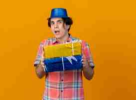 Foto gratuita impresionado apuesto hombre caucásico vestido con gorro de fiesta azul tiene cajas de regalo