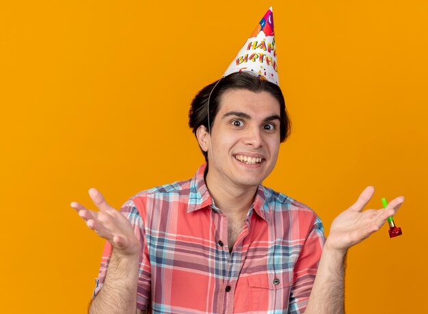 Impresionado apuesto hombre caucásico vistiendo gorro de cumpleaños tiene silbato de fiesta