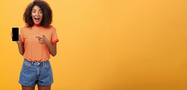 Foto gratuita impresionado fascinado elegante delgado afroamericano mujer de cabello rizado en camiseta a rayas dejando caer la mandíbula