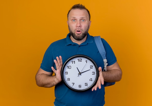 Impresionado hombre adulto eslavo con mochila sosteniendo el reloj