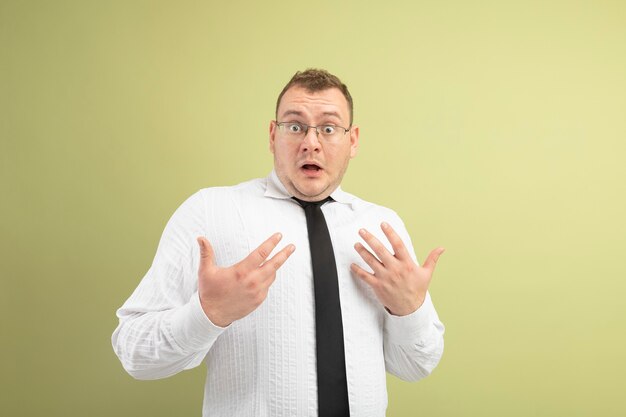 Impresionado hombre eslavo adulto con gafas y corbata mirando a la cámara apuntando a sí mismo con las manos aisladas sobre fondo verde oliva con espacio de copia