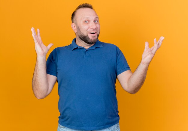 Impresionado hombre eslavo adulto y manteniendo las manos en el aire aislado en la pared naranja