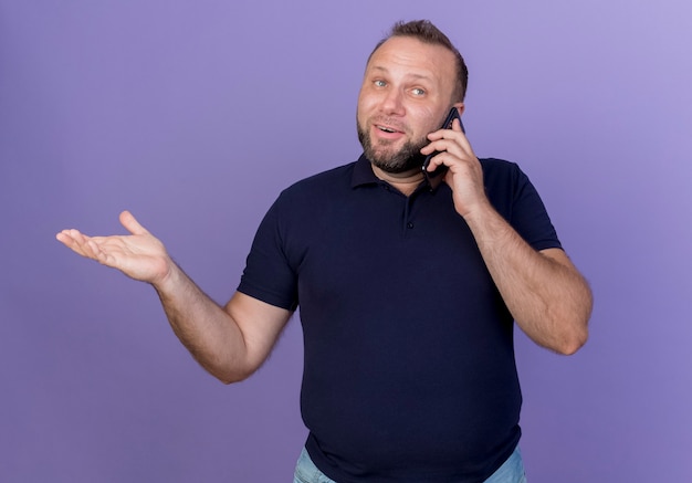 Impresionado hombre eslavo adulto mirando al lado hablando por teléfono mostrando la mano vacía aislada