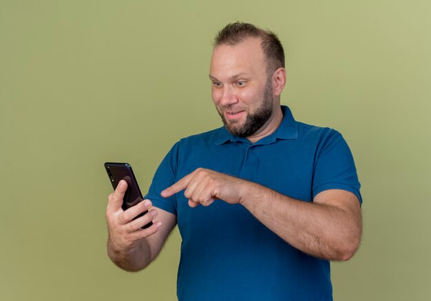 Impresionado hombre eslavo adulto sosteniendo apuntando y mirando el teléfono móvil