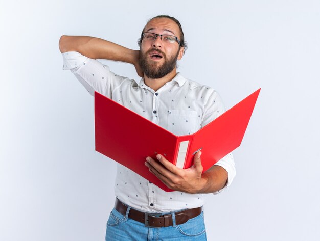 Foto gratuita impresionado hombre guapo adulto con gafas sosteniendo una carpeta abierta manteniendo la mano detrás del cuello