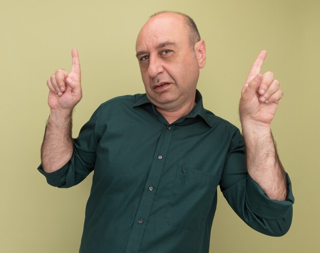 Impresionado hombre de mediana edad con camiseta verde apunta hacia arriba aislado en la pared verde oliva